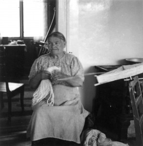 Eldre dame, Anne H. Blomsterli sitter på en stol og lager innslagsdukker/uddu til greneveven.